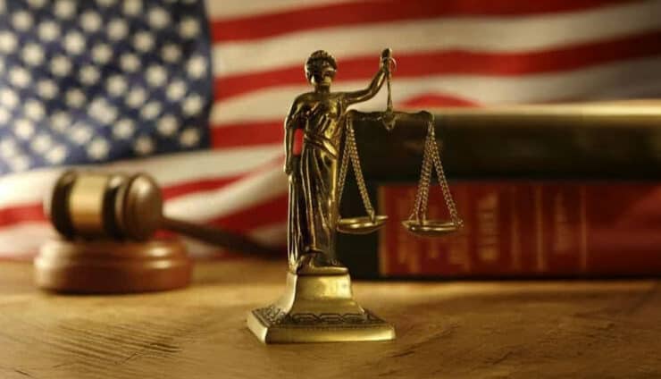 legal image of legal books, just is blind staute with scales, on a wood desk and american flag in background